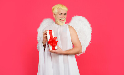 Valentines day celebration. Smiling bearded man in angel wings with Valentine gift. Male cupid in...