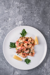 Fried Argentine shrimps with garlic and herbs on a white plate with lemon, view from above.