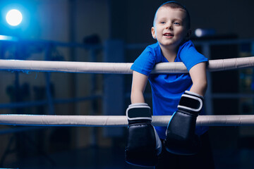 Portrait boy in black boxing gloves is training in ring, sport kid boxer tired in gym.
