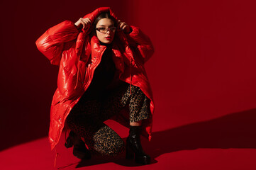 Fashionable confident woman wearing trendy oversized red puffer down jacket, sunglasses, leopard...
