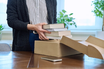 Close-up of woman's hands unpacking cardboard box with new books - obrazy, fototapety, plakaty