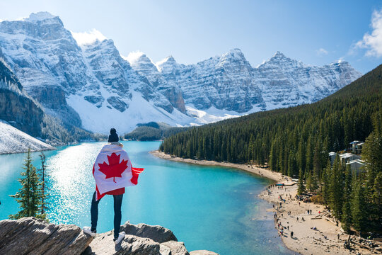 Tourist draped in Canadian flag looking beautiful scenery of Moraine lake. Banff National Park. Canadian Rockies. Alberta, Canada.