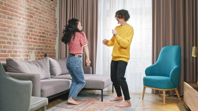 Cute Caucasian family dancing barefoot on carpet in middle of living room of modern apartment. Povitive vibes. Enjoying free time and goofing around. Moving their bodies to rhythm.
