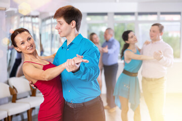 Portrait of positive adult pairs of different ages enjoying tango in modern dance hall together