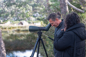 A man and a woman bird watching in the lake with a telescope.