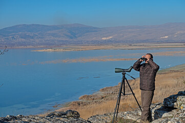 A man with binoculars bird watching on the lake.