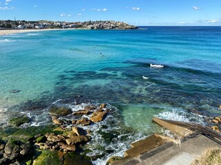 Bay and coastline close to the ocean. View of the city in the distance. Turquoise waves breaking on the rocky shore and tidal pool. Australia, Sydney landscape.