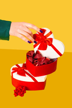 Anonymous hand opening a heart-shaped gift box with red ribbons on a yellow background
