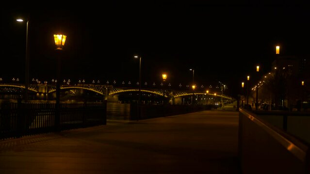 Danube river in budapest during night time. A view of empty road by Danube river with illuminated bridge against night cityscape.