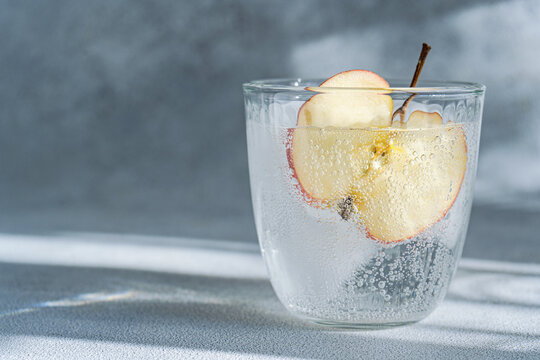 A close-up view of a glass of tonic water with a slice of apple, highlighting the drink's bubbles and refreshing appearance
