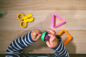 Manos de niña de  2 años jugando con plastilina casera y moldes. Jugar con la plastifica en casa, juguetes educativos para niños Montessori. Juegos creativos para niños pequeños. 