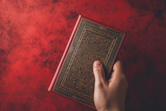 Hand Clasping A Richly Decorated Quran Against a Deep Red Background in the Holy Month of Ramadan Created With Generative AI Technology