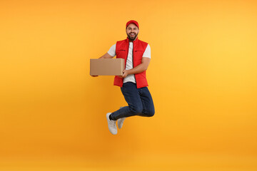 Happy young courier jumping with parcel on orange background
