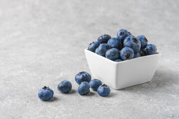 Fresh blueberries in a small square bowl on gray concrete background with copy space. Organic berries, healthy food, wild berries