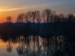 Spring flood, sunset landscape with flooded trees and reflection in the water