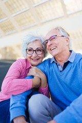 Vertical photo of a happy elder couple sitting and embracing in an urban space