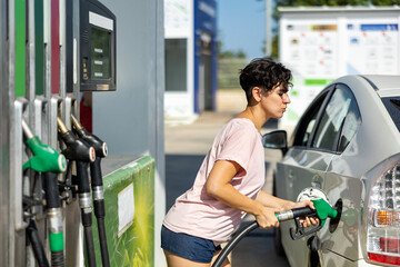 Cheerful latin woman using nozzle to refuel her car in gas station