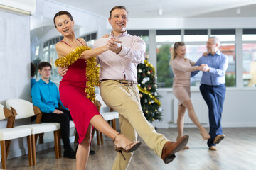 Happy brunette in stylish red dress decorated with golden tinsel dancing energetic upbeat jive...