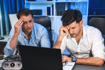 Stressful business partner with headache analyzing paperwork project together on desk at night time of startup product company. Concept of overworked design on neon blue light modern office. Sellable.