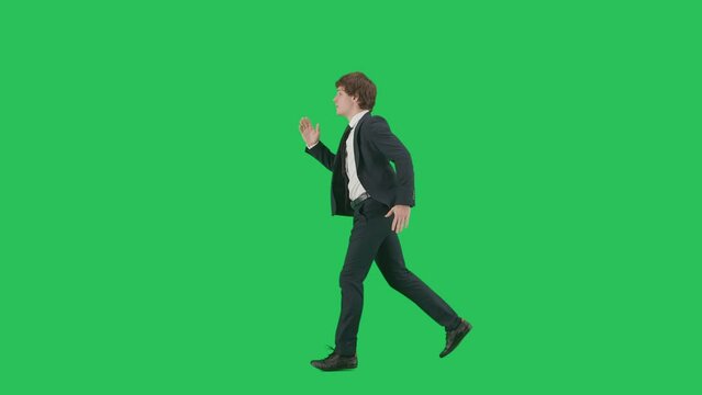 Profile view of male model in suit isolated on chroma key green screen background. Positive young businessman in blue suit running fast.