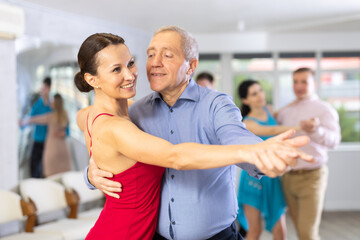 Fototapeta na wymiar Positive people of different ages dancing tango in pairs in dance hall