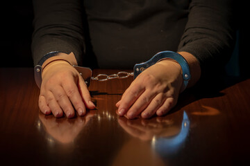 The woman's hands are on the table and handcuffed. Concept: female criminality, interrogation by an...