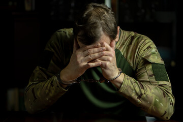 A military soldier in handcuffs gives evidence during interrogation, hiding his face.