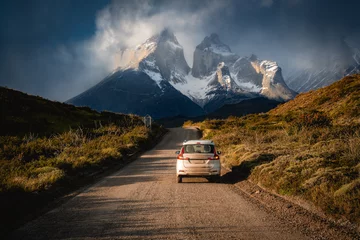 Foto op Plexiglas Cuernos del Paine a car on a road to the snow mountain under clouds and sun light