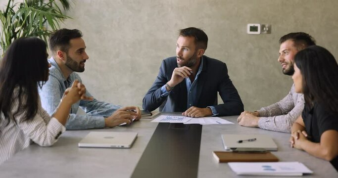 Five diverse company members gather in boardroom, sit at desk, listen team leader boss, solve joint business, analyzing strategy, planning project launch, do sales analysis. Briefing, communication