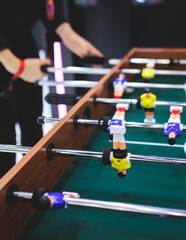 Group of friends playing kicker in a sports bar room, colleagues teammates play table football, table soccer game in the office, having fun, tabletop football match competition at work - obrazy, fototapety, plakaty