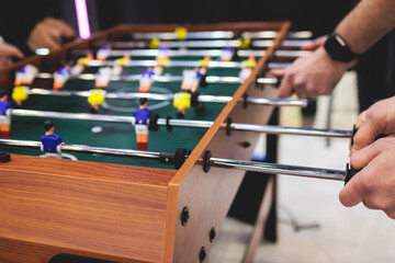Group of friends playing kicker in a sports bar room, colleagues teammates play table football,...