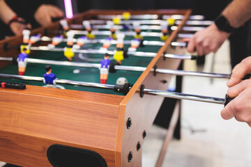 Group of friends playing kicker in a sports bar room, colleagues teammates play table football,...