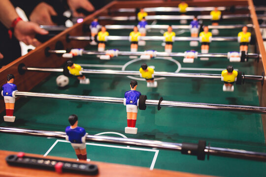 Group of friends playing kicker in a sports bar room, colleagues teammates play table football, table soccer game in the office, having fun, tabletop football match competition at work