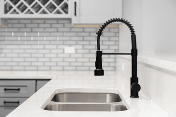 A kitchen faucet detail with grey cabinets, grey glass subway tile backsplash, and black faucet.