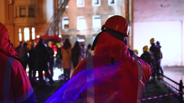 Group of fire men in protective uniform during fire fighting operation in the night city streets, firefighters brigade with the fire engine truck vehicle, emergency and rescue service