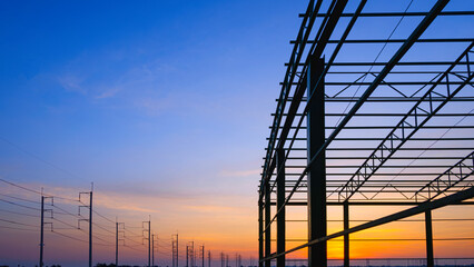 Silhouette metal warehouse outline structure in construction site with row of electric poles in...