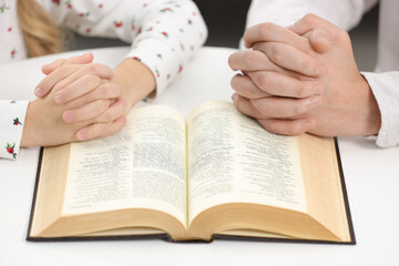 Fototapeta premium Girl and her godparent praying over Bible together at table indoors, closeup