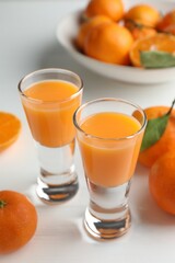 Tasty tangerine liqueur in shot glasses and fresh fruits on white table