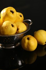 Tasty ripe quinces and metal colander on black mirror surface, closeup