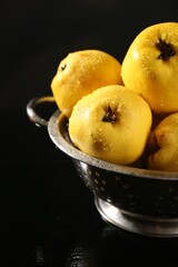 Naklejka na ściany i meble Tasty ripe quinces with water drops in metal colander on black background, closeup