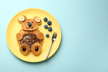 Creative serving for kids. Plate with cute bear made of pancakes, blueberries, bananas and chocolate paste on light blue table, top view. Space for text - obrazy, fototapety, plakaty