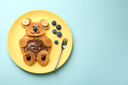 Naklejki Creative serving for kids. Plate with cute bear made of pancakes, blueberries, bananas and chocolate paste on light blue table, top view. Space for text