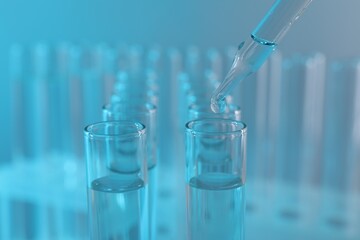 Laboratory analysis. Dripping liquid from pipette into glass test tube on light blue background, closeup