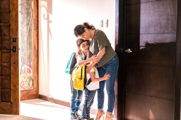 Mother hugs her children with a lot of love at the door of her house upon their arrival from school.