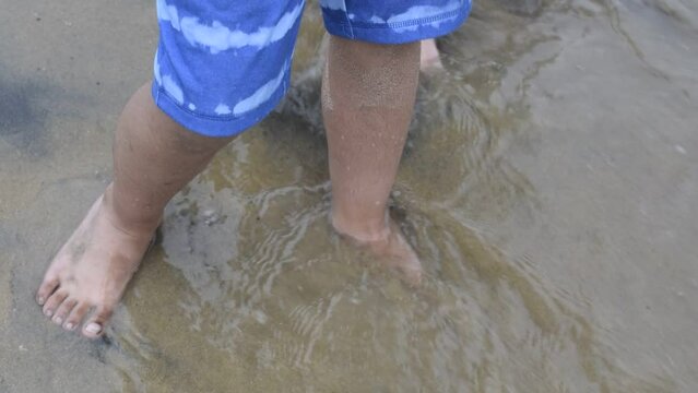 Kids standing barefoot on a sea shore with waves crashing. They are enjoying barefoot on the sand
