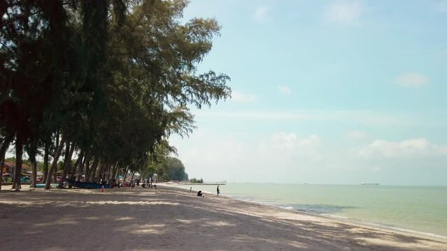Cinematic footage of Pantai Puteri Beach in Melaka, Malaysia, during a partly cloudy day. People are seen enjoying the shoreline, having picnics, and having fun.