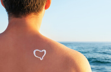 smear of sunscreen in the shape of heart on male back against the sea, rear view.