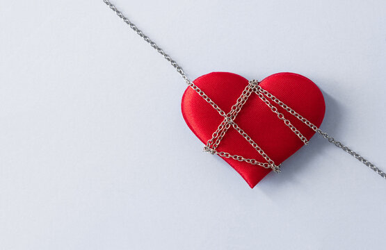 Red heart bound with metal chains.Concept of domination, manipulation and abuse in relations. Selective focus, copy space