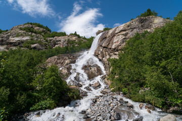 Obraz premium View of the Alibek waterfall formed by the fall of the Jalovchatka River from the Alibek glacier on a sunny summer day, Dombay, Karachay-Cherkessia, Russia