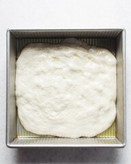 Focaccia dough rising in a square baking pan, process of making focaccia, bread dough rising in a baking pan